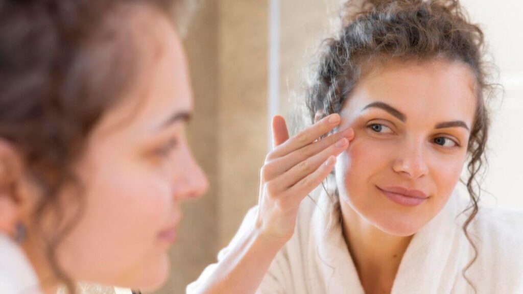 Mulher em frente ao espelho passando creme ao redor dos olhos como tratamento para olheiras