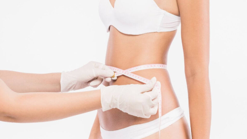 Cirurgião com luvas mede cintura de paciente com fita métrica
