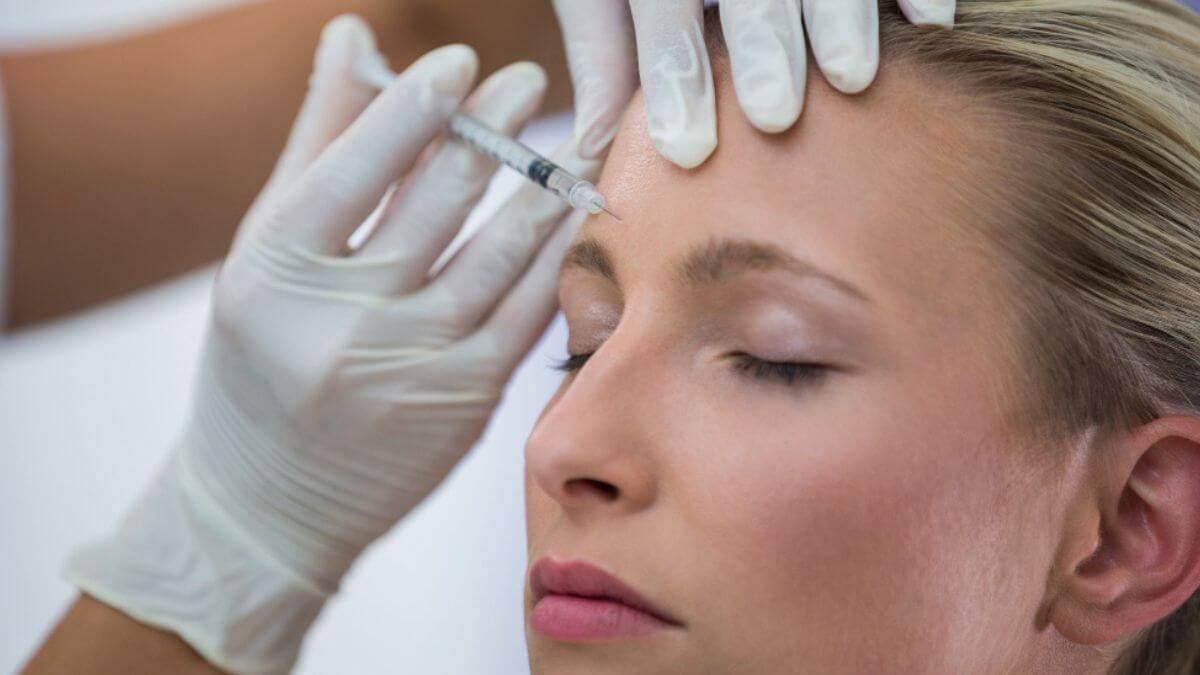 Mulher com olhos fechados recebendo aplicação de botox para tratar as rugas na testa